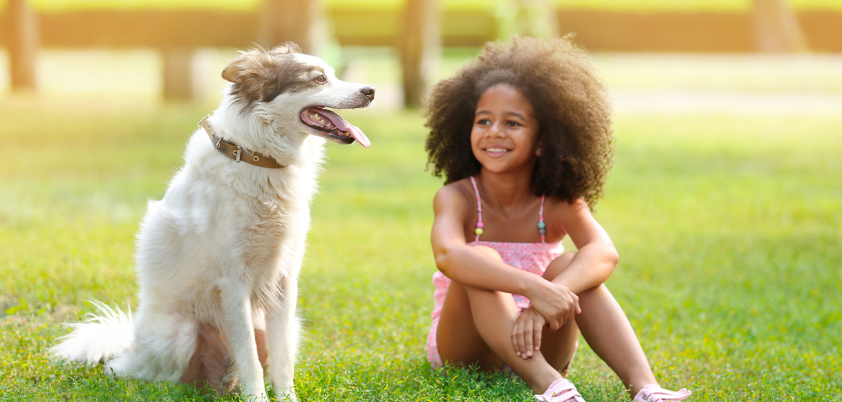 little girl and a dog sitting on green grass